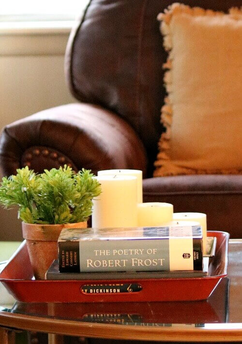 A coffee table with a tray full of decor, such as two books, candles, and greenery in a pot.