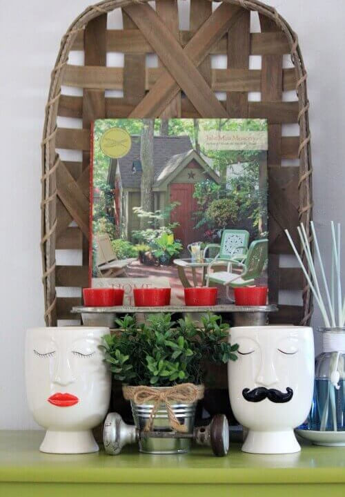 A tobacco basket on the wall with a gardening book placed inside. Red votives in a muffin tin, two vases (man and woman) a plant, and an old door knob.