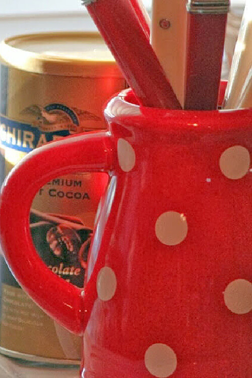 A red and white polka dotted creamer with spoons inside.