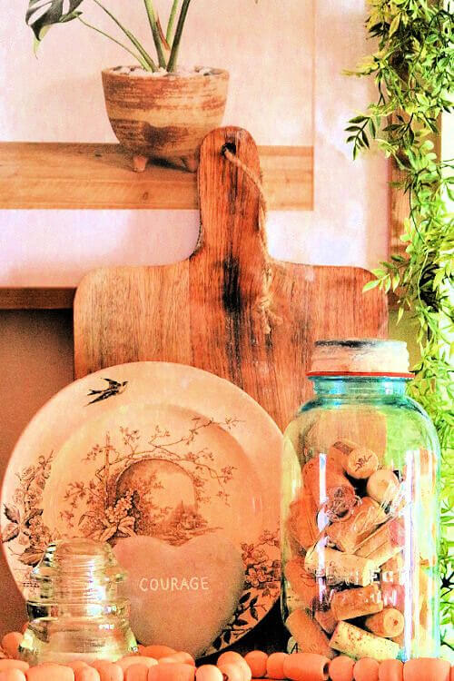 A neutral brown setting with a house plant painting on the well, a weathered cutting board, and a plate and jar of wine corks.