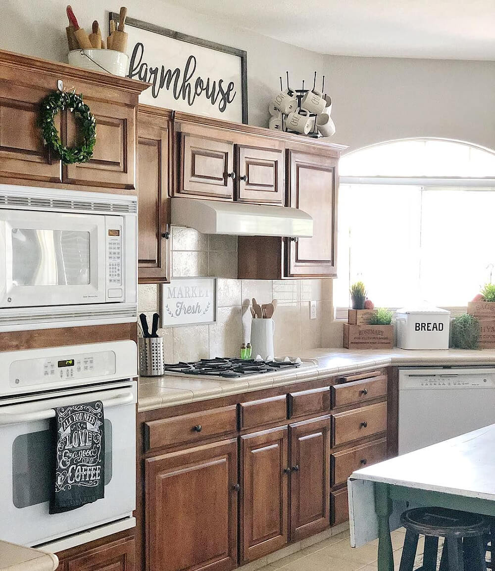 In how to style space above kitchen cabinets, this one is styled with a farmhouse sign, a collection of vintage rolling pins, and coffee mugs.