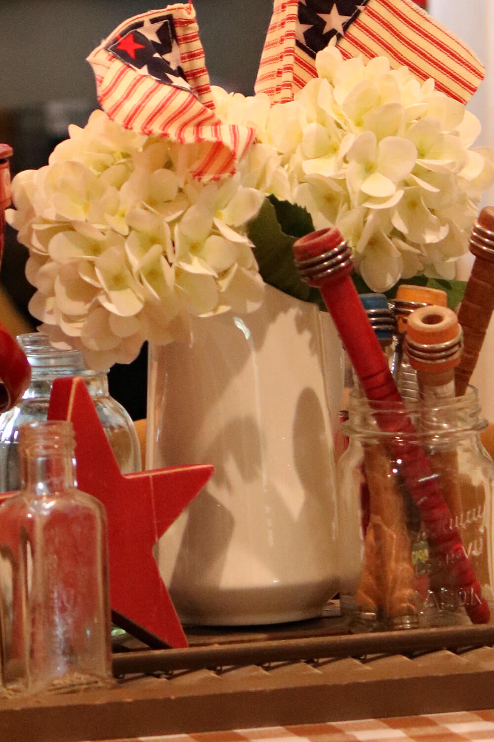 Celebrate July 4th with cozy cottage charm with white hydrangeas in a white pitcher and red, white, and blue wood bobbins in a vintage jar.