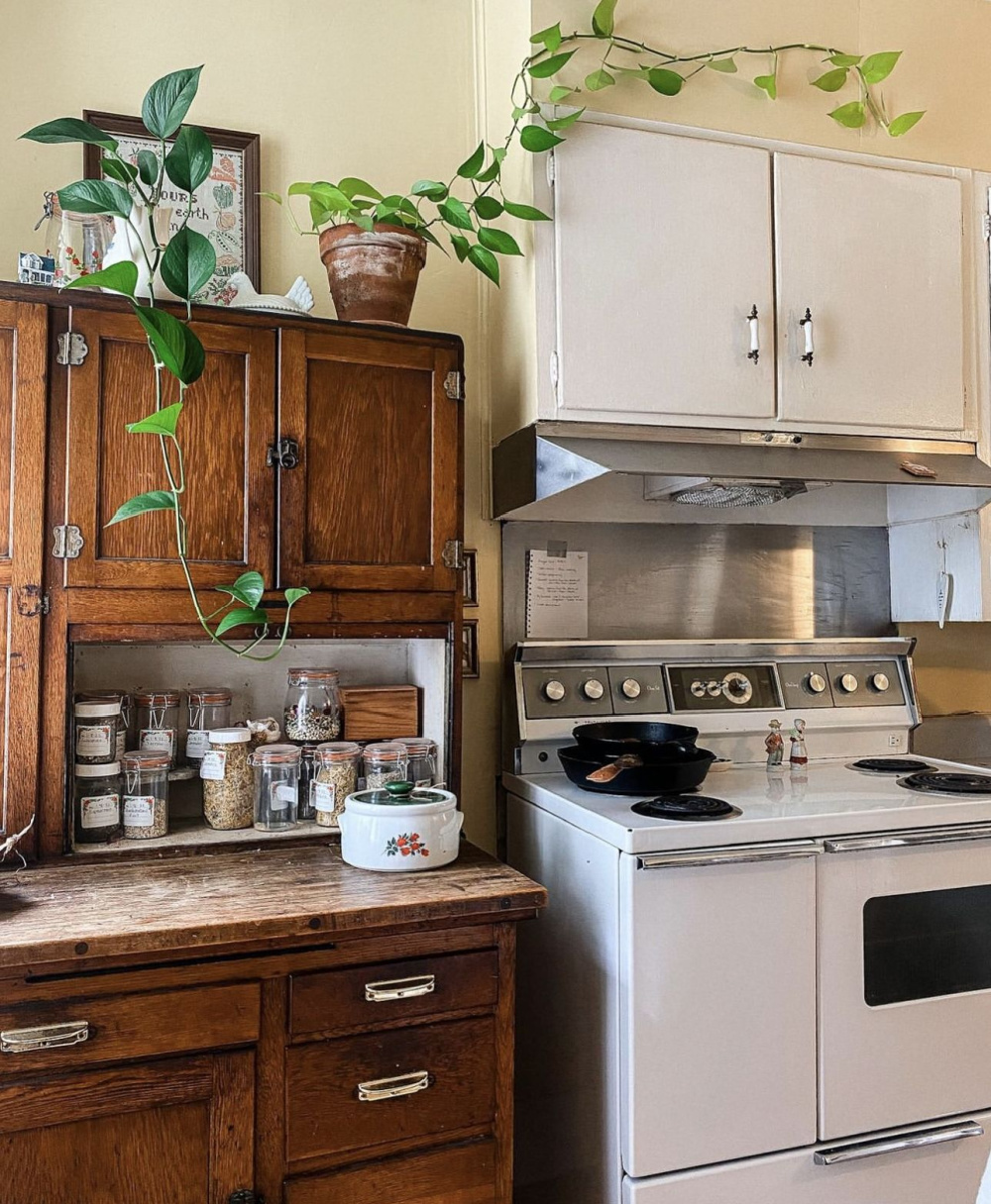 This kitchen with white stove has an antique cupboard standing next to it.
