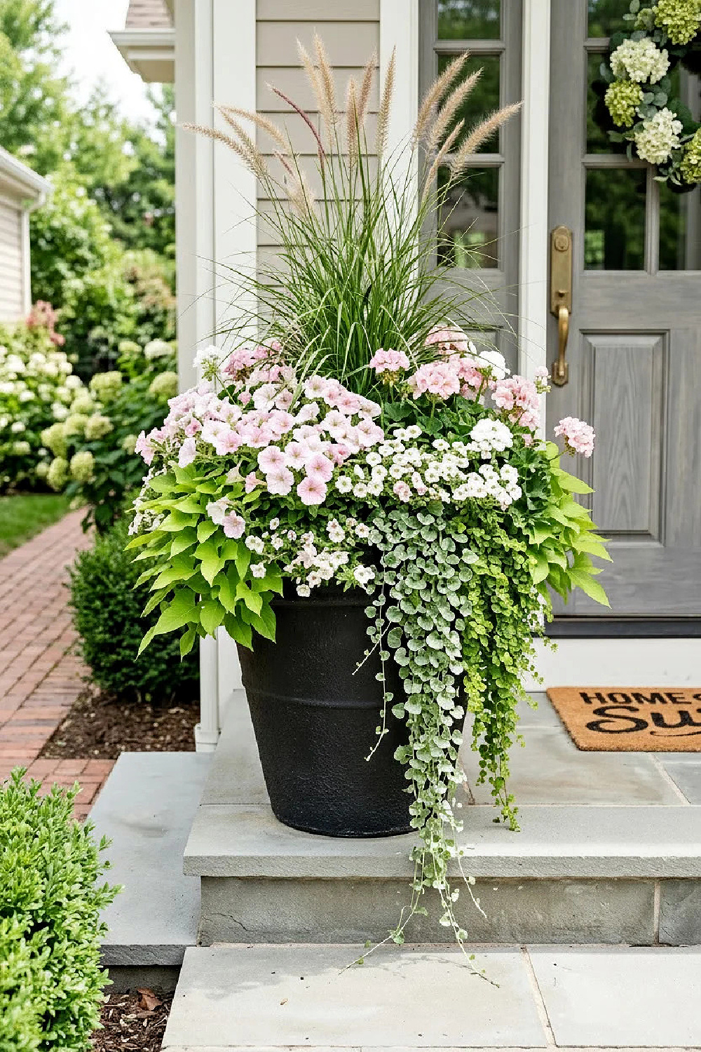 25 Pretty Porch Planters That Boost Curb Appeal include this stunning tall black pot with a variety of plants spilling over. 