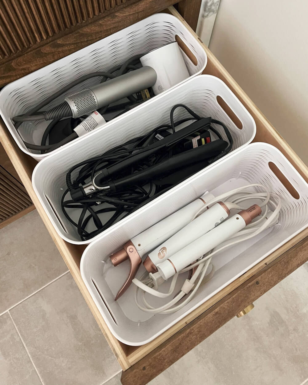 Plastic bins inside a drawer hold electrical hair dryers and curling irons.