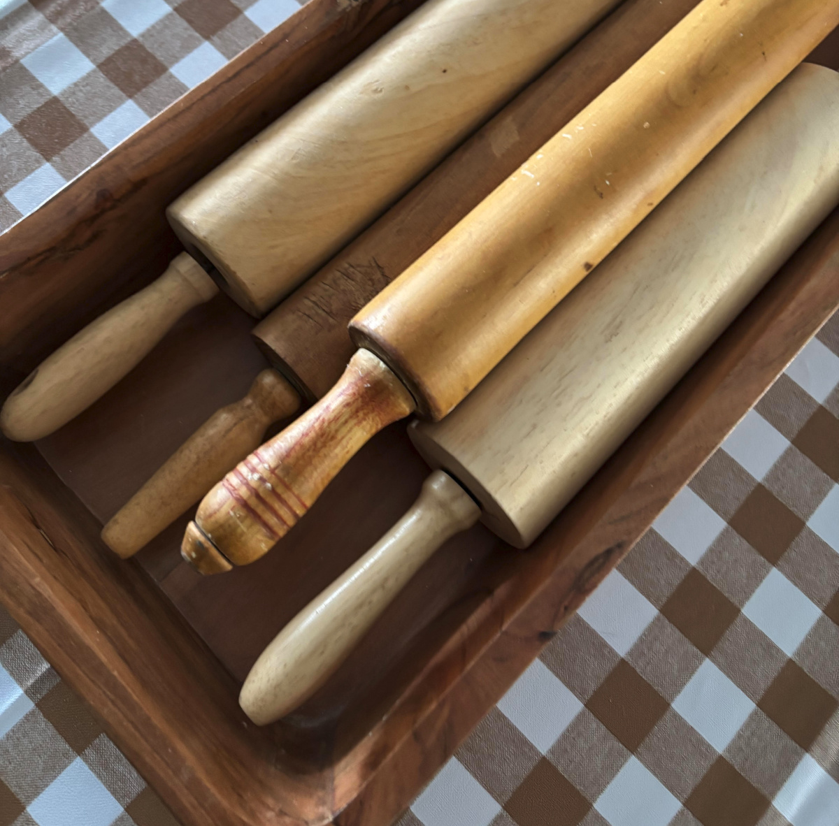 Vintage rolling pins in a wooden tray on my dining table covered with a brown and white tablecloth.