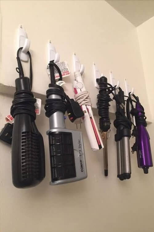 In 26 Bathroom Storage Ideas for Small Spaces, adhesive hooks hold hair dryers and curlers.