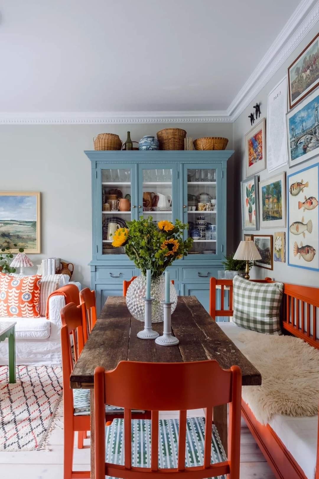A brown slatted bench, a rustic brown table, and four matching chairs surrounding it. A blue kitchen hutch is against the wall near it.