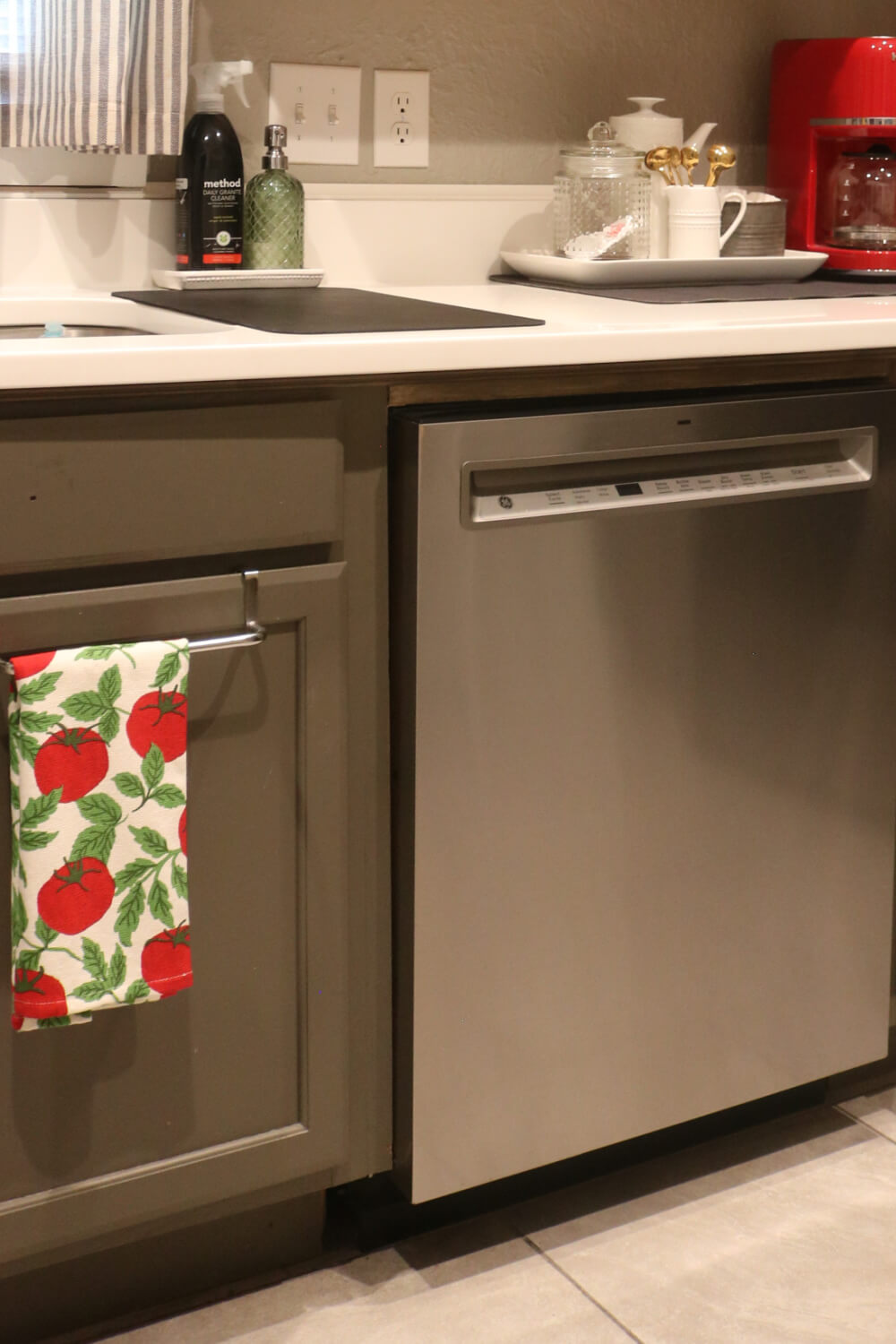 My stainless steel dishwasher and a tomato-themed dish towel hanging on an over the cabinet door dish hanger.