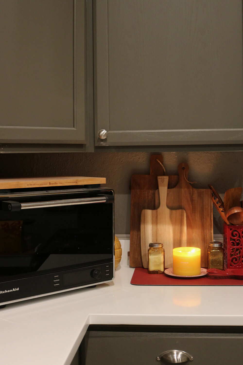 Simple ways to add yellow to your kitchen with a lemon drop candle in front of beautifully textured cutting board and a red container for wood utensils.