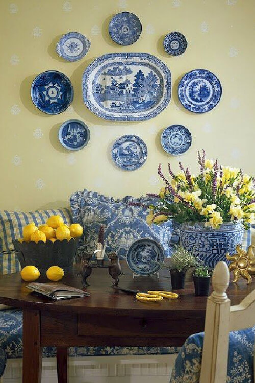 This is an evenly spaced blue and white plate wall. Underneath is a table with a settee and pillows.