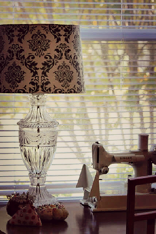 Summing up life in the 1960s, clothing were often sewed on a Featherweight Singer sewing machine like the one next to this clear glass lamp with a green and beige shade.