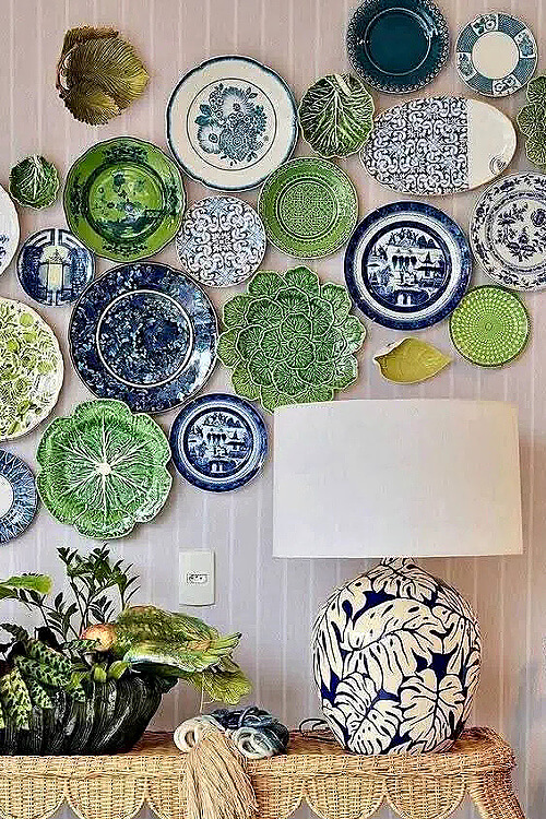 A blue, white, and green plate wall. Underneath is a large blue and cream botanical lamp and a house plant.