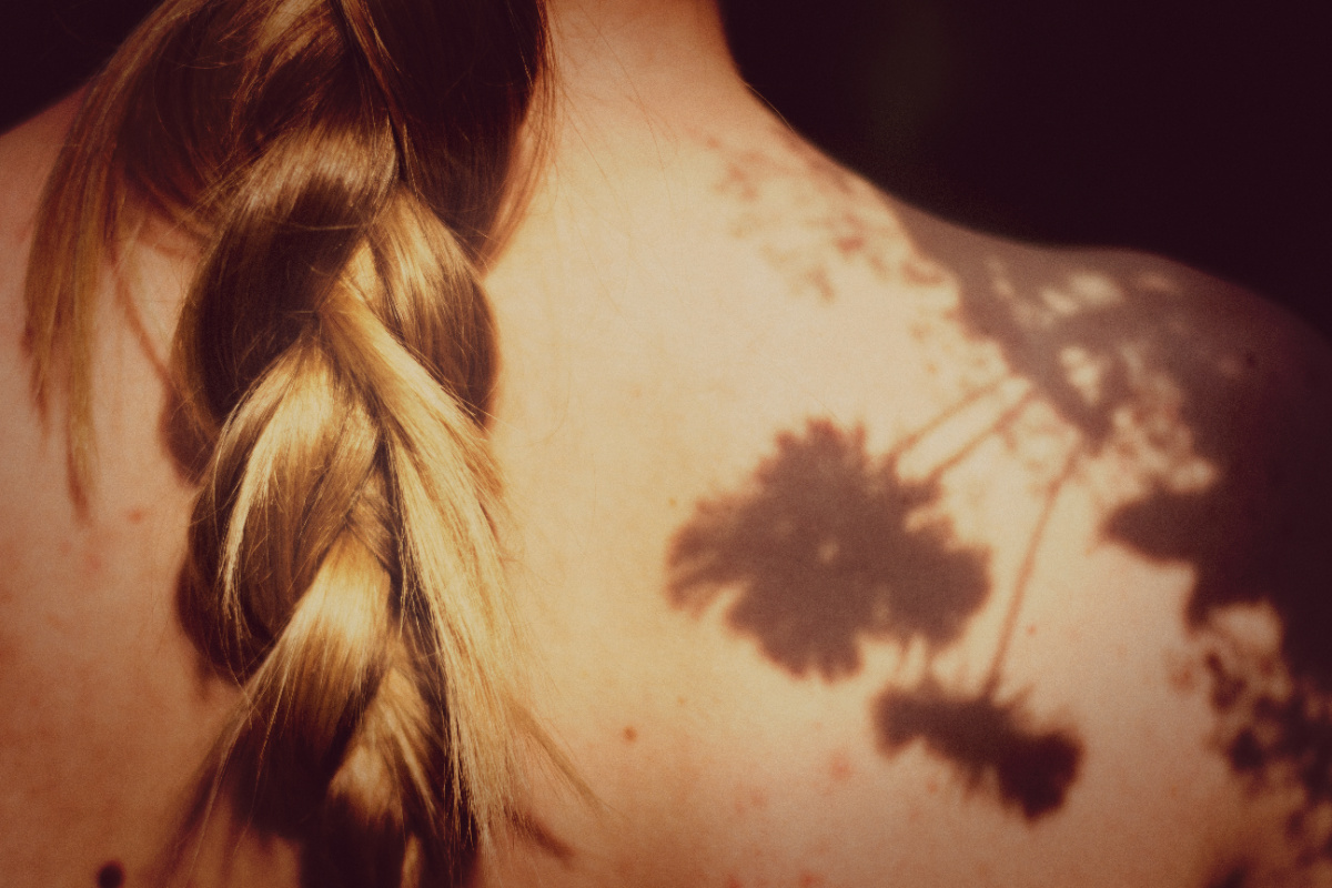 A woman with a blond braid with her back to the camera and sun shining on her back.