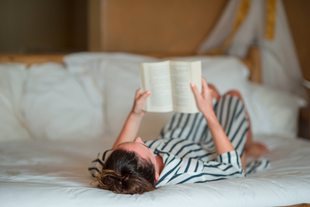 Woman reading a book lying in bed.