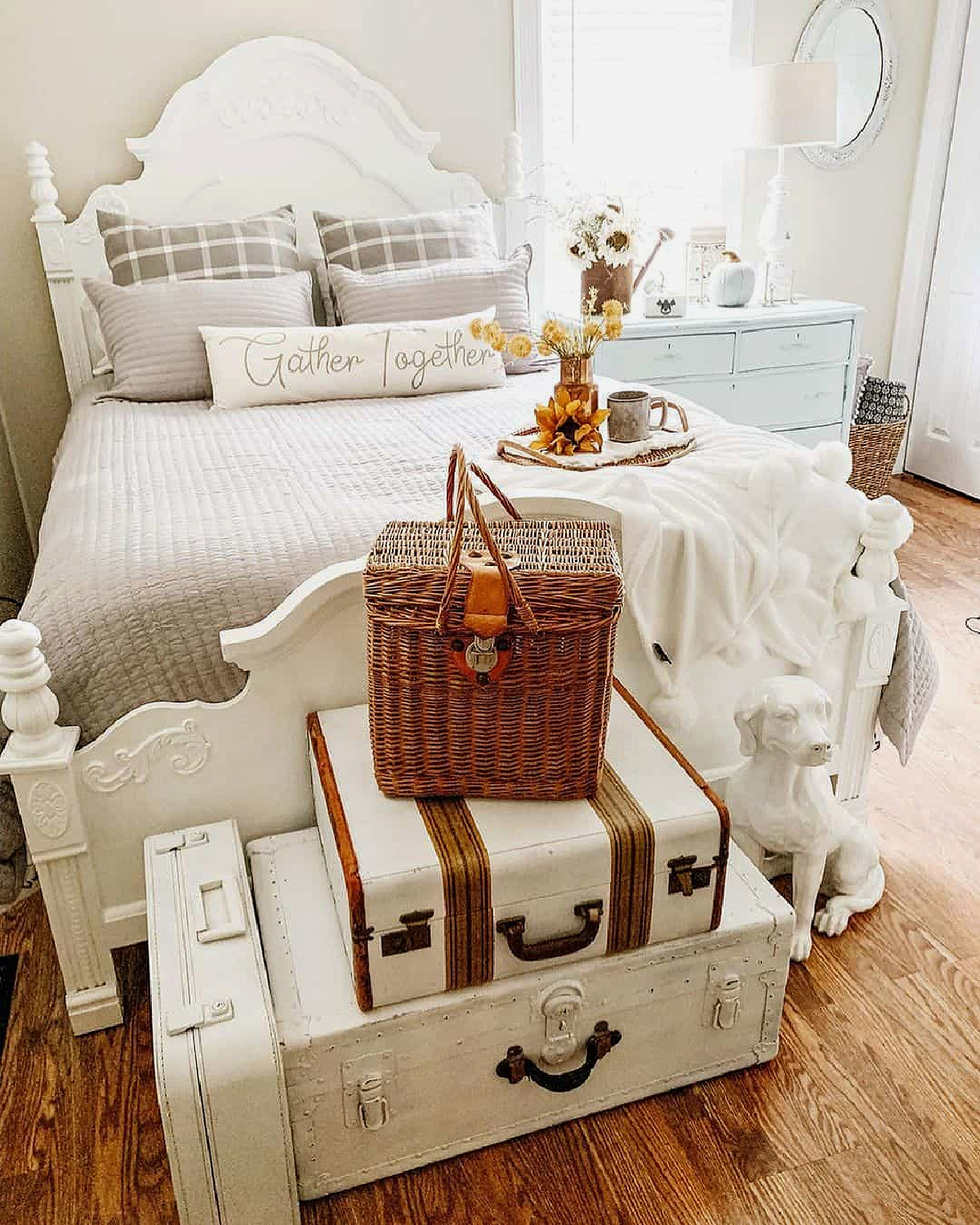 22 ideas to repurpose vintage suitcases includes this repurposed stack at the end of a white bed. A white sculptural dog sits next to it.