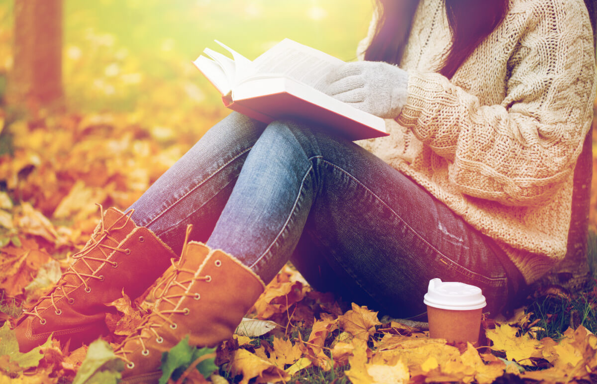 The books I'll be reading this fall and winter, with a woman reading out on a fall day with autumn leaves.