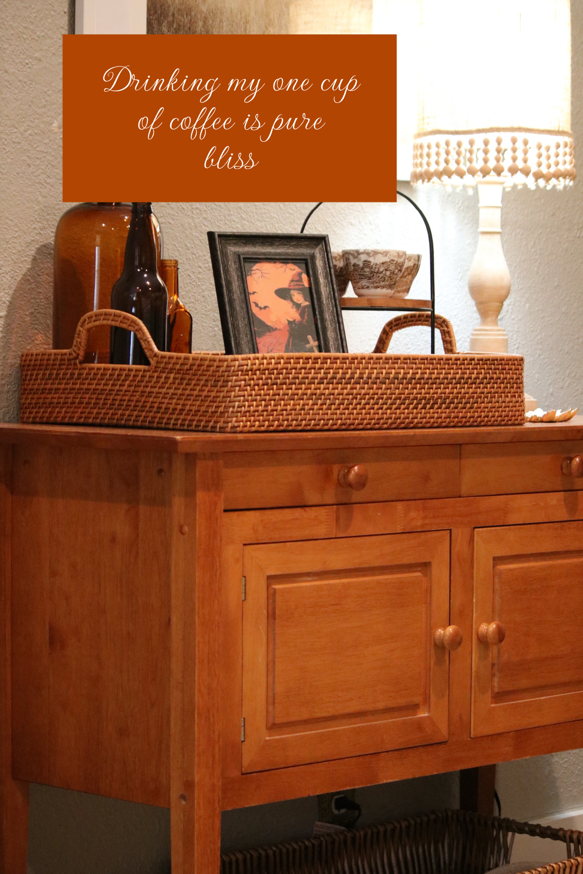 Drinking my one cup of coffee in my living room where the wooden cupboard has decor on the surface.