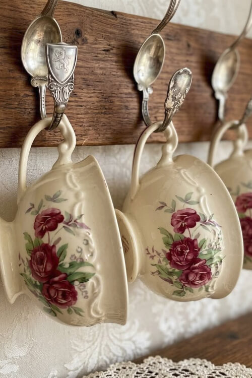 Teacups hanging from vintage spoons formed into hooks and attached to wood.