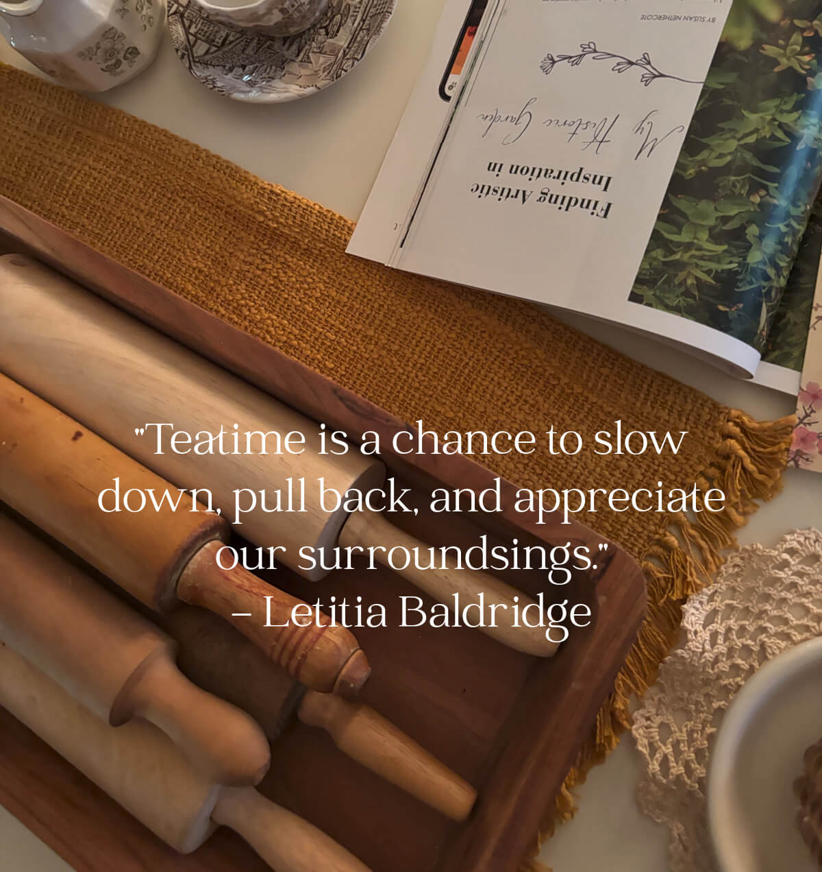 A table with an open magazine, a brown and white transfer ware teacup and dish, and a wooden bowl of vintage rolling pins.