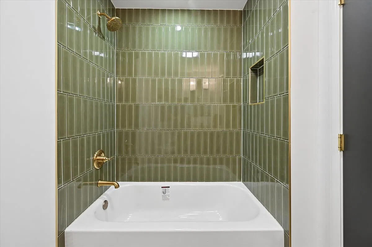 The other bathroom with olive green tiles surrounding the bathtub.